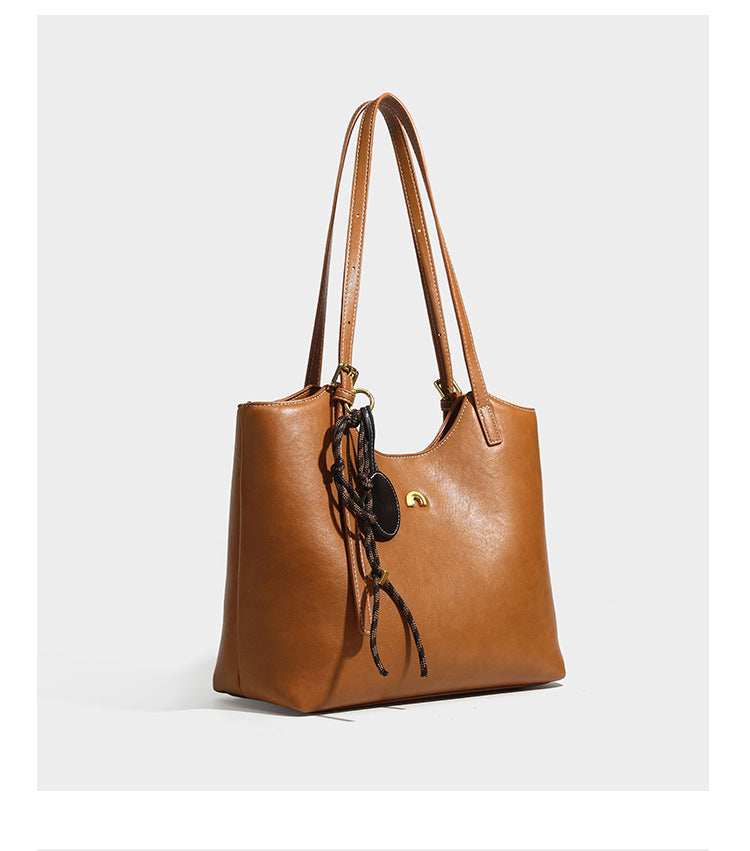 Structured smooth leather-look tote bag with long shoulder strap, gold-tone hardware, and hanging tassel-coin charm, detail