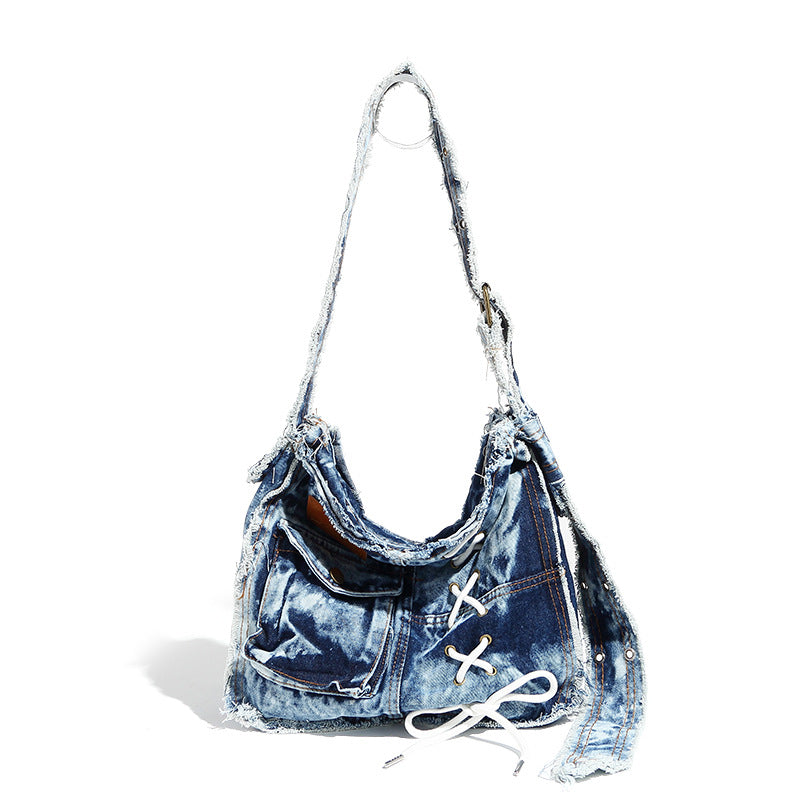 Slouchy distressed denim shoulder bag with frayed edges, white lace-up cross detail, front snap pocket, and long shoulder