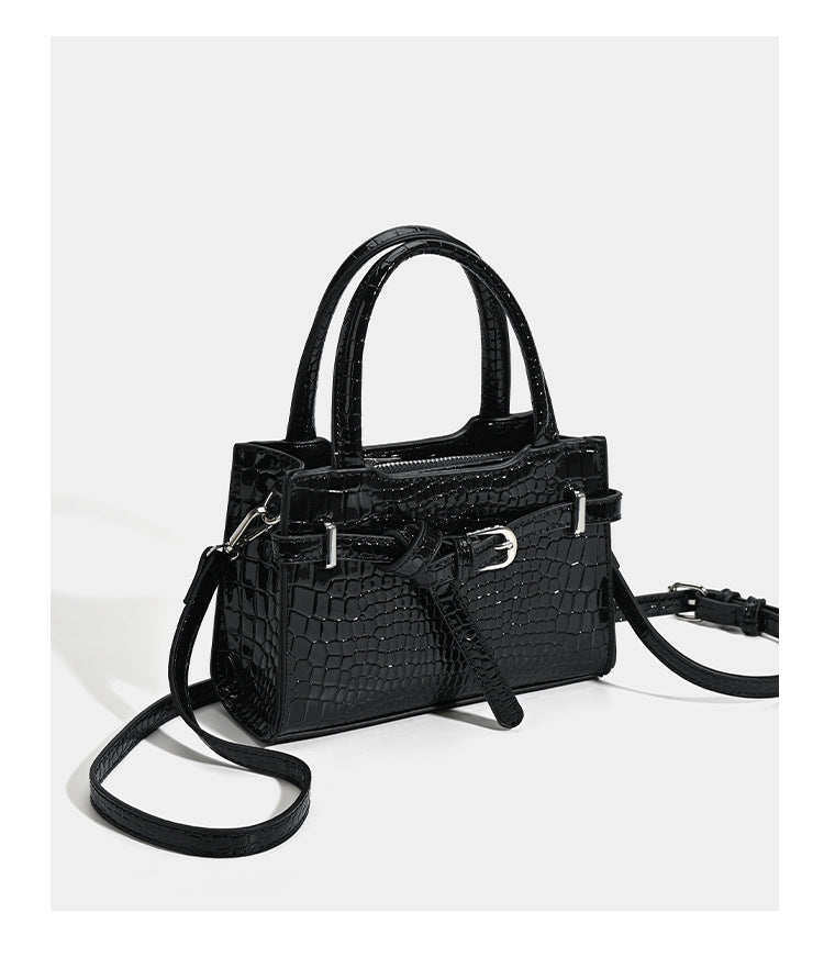 Small structured trapezoid mini top-handle bag with front belt-knot buckle detail and glossy leather-look finish, detail view