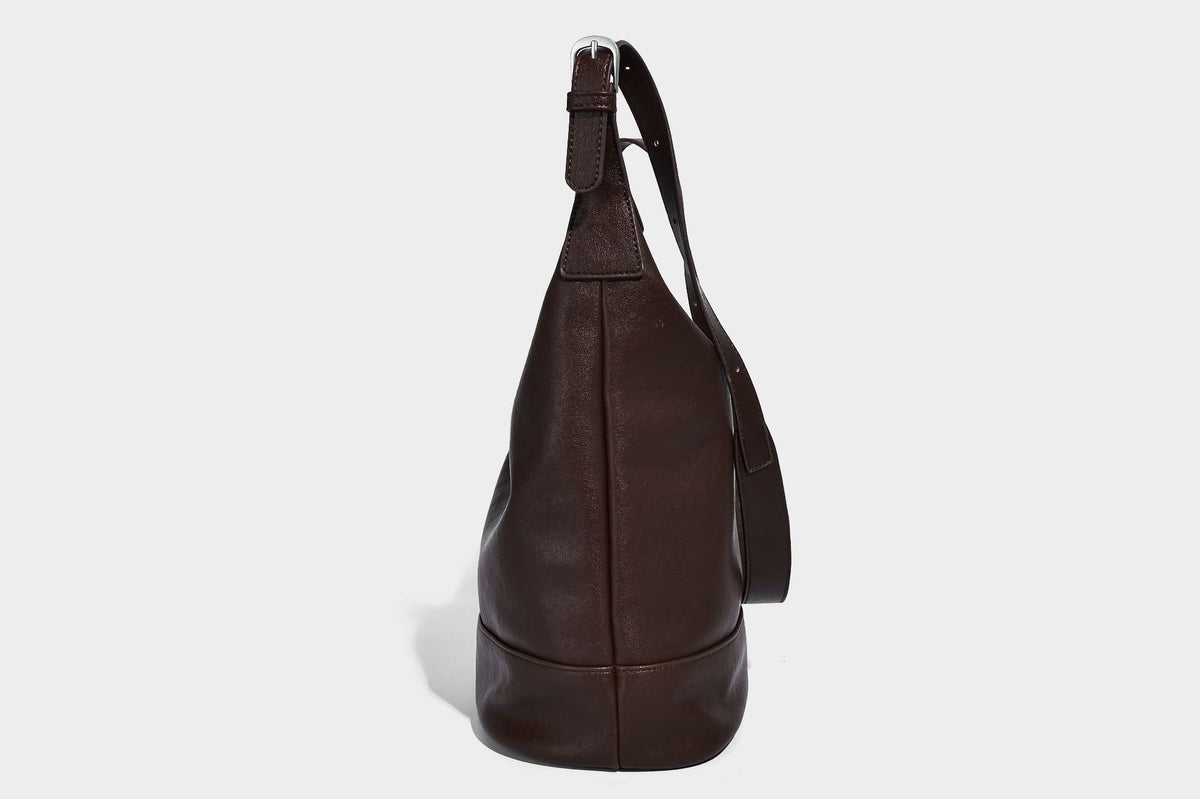 Slouchy bucket hobo shoulder bag in dark brown with glossy leather-look finish, top zip closure, and long adjustable, detail