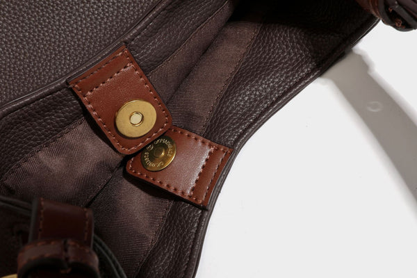 Hobo-Schultertasche in dunklem Espresso mit genarbter Oberfläche, warmen cognacfarbenen Details, verstellbarem schmalem Riemen, goldfarbenen Ringbeschlägen und geknotetem