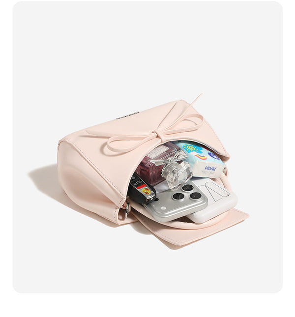 Small structured trapezoid handbag with a three-dimensional front bow, short top handle, and detachable shoulder strap