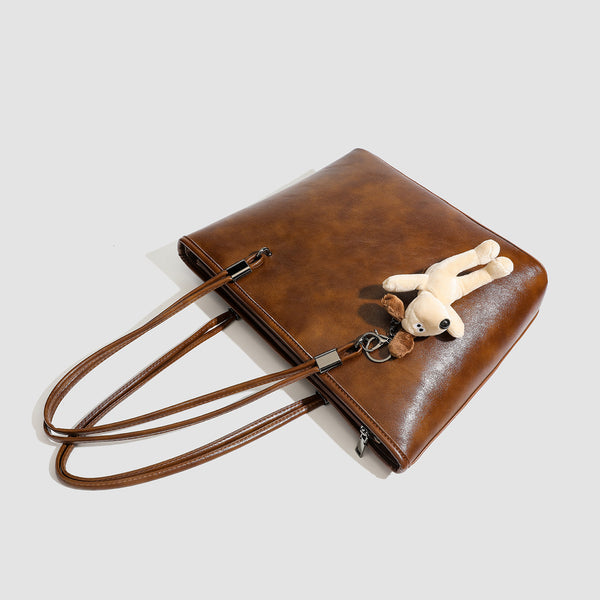 Large structured brown vintage-finish tote bag with double shoulder handles, gunmetal hardware, and plush bear charm, detail
