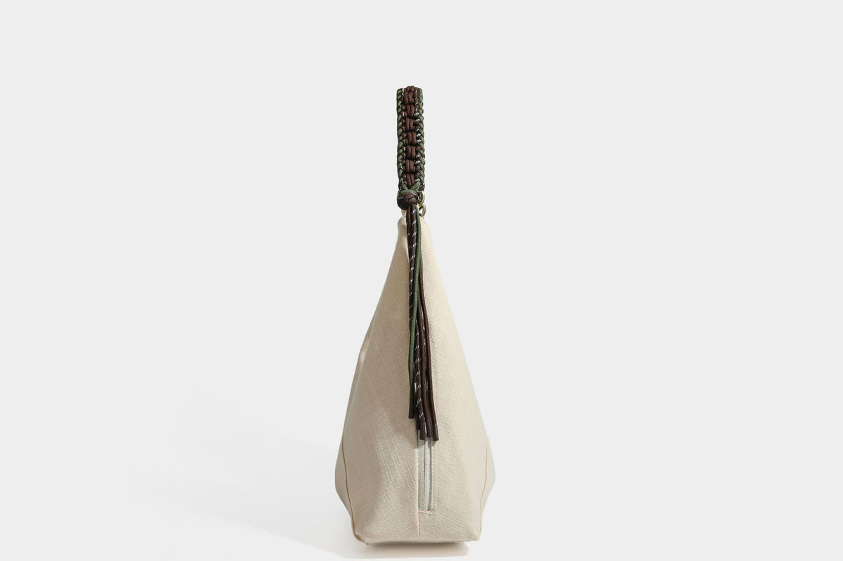 Soft slouchy cream canvas shoulder tote with braided brown and green cord handle, gold-tone ring hardware, and tassel trim