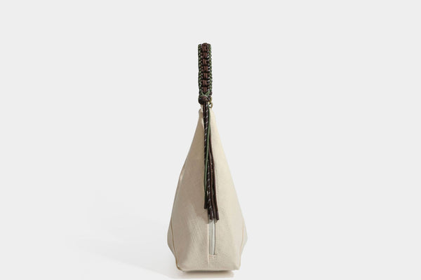 Soft slouchy cream canvas shoulder tote with braided brown and green cord handle, gold-tone ring hardware, and tassel trim