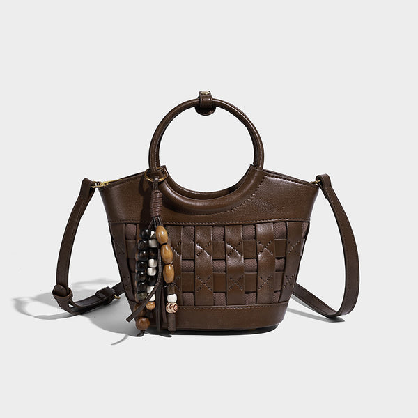Small woven-panel bucket bag with circular ring handles, beaded tassel charm, and detachable crossbody strap in brown, detail