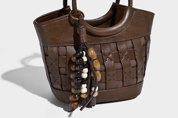 Small woven-panel bucket bag with circular ring handles, beaded tassel charm, and detachable crossbody strap in brown, detail