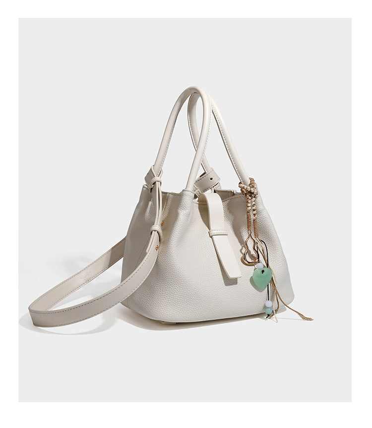 Pebbled leather-look bucket tote bag with rolled double handles, drawstring closure, braided cord charm, and detachable