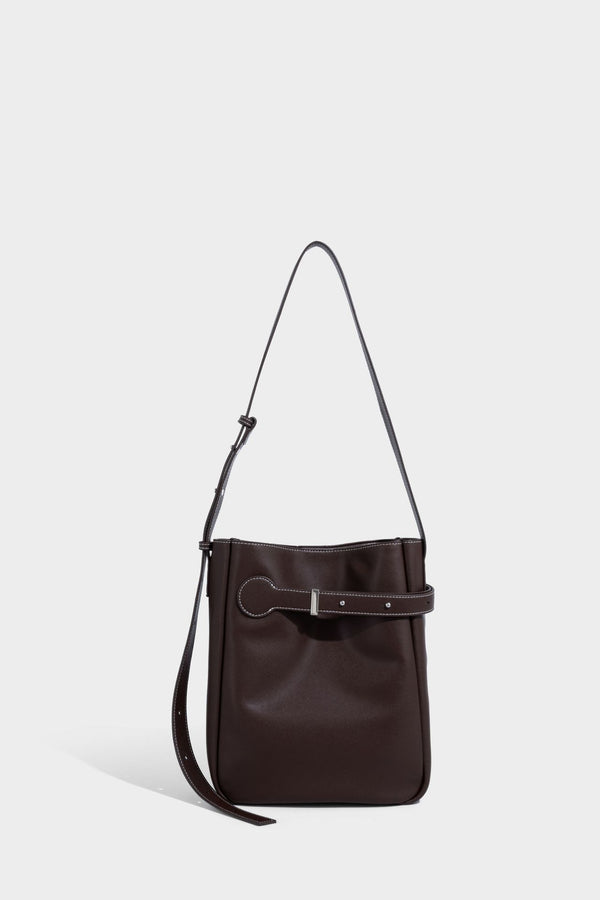 Structured dark brown leather-look bucket bag with white contrast stitching, front wraparound belt buckle strap, and long