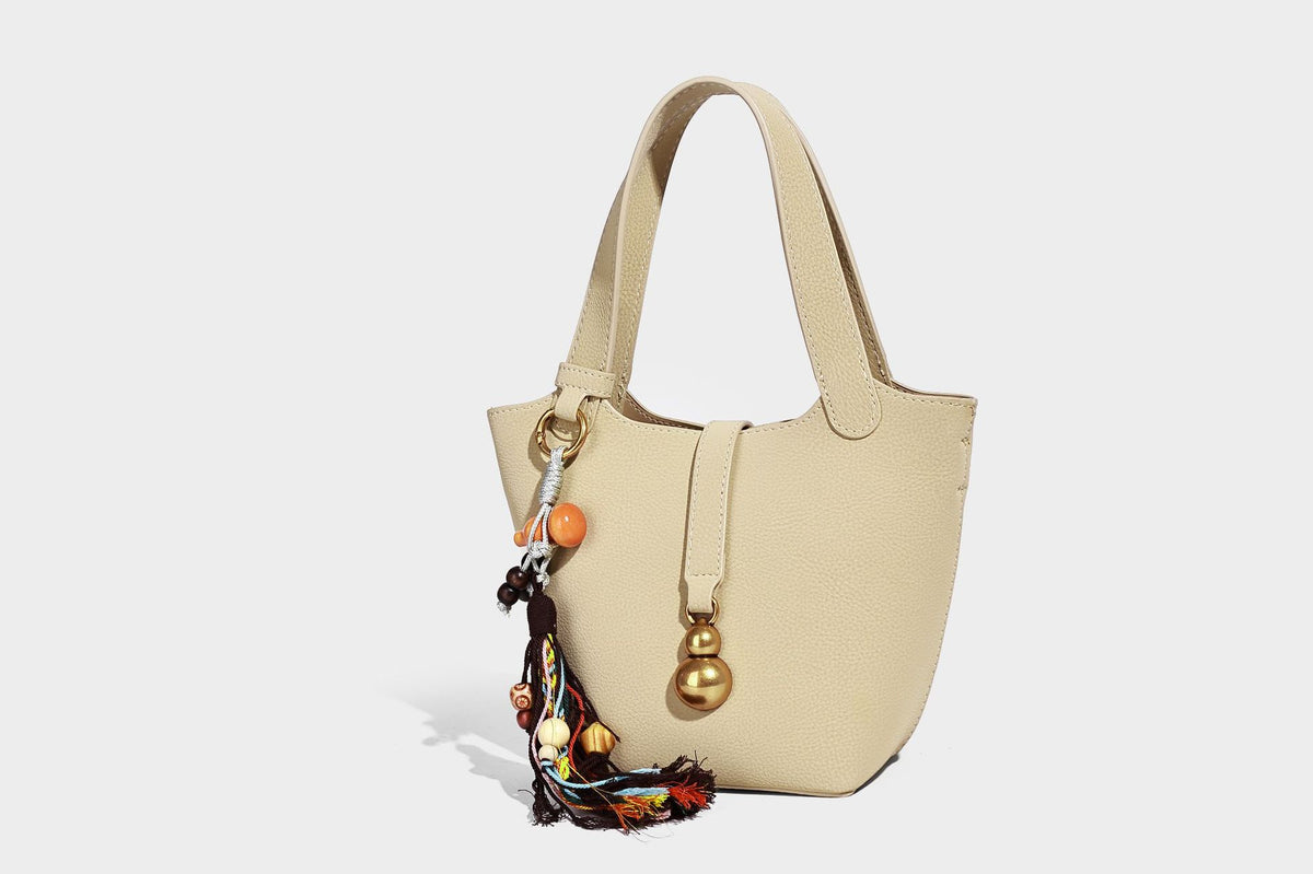 Kleine matte Beuteltasche mit genarbter Oberfläche, antikgoldfarbenen Ringbeschlägen, Perlen- und Quastenanhänger, kurzen Tragegriffen oben und