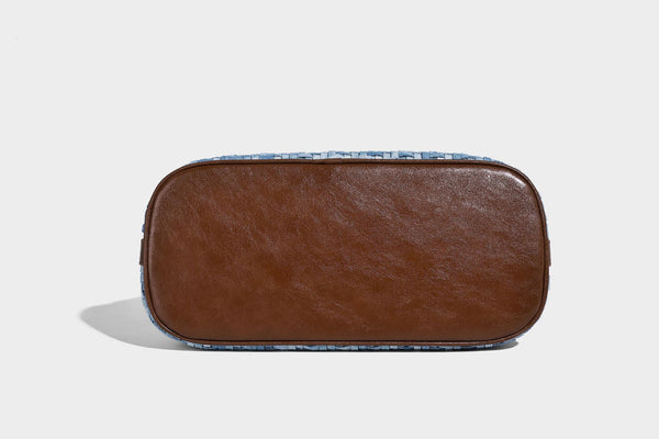 Light blue woven bucket bag with brown leather-look trim, gold-tone hardware, adjustable shoulder strap, and decorative bead