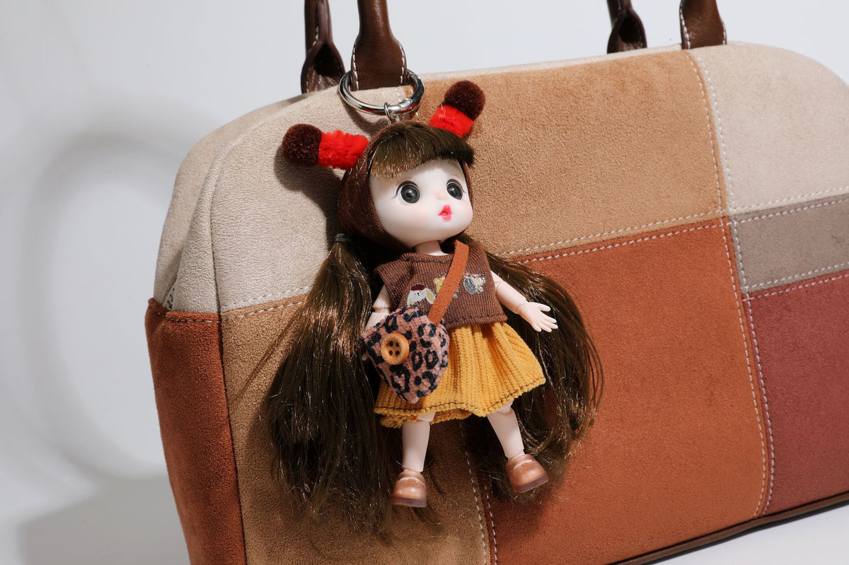 Boxy patchwork suede-look shoulder tote in tan, beige, rust, and brown panels with double brown straps and hanging doll