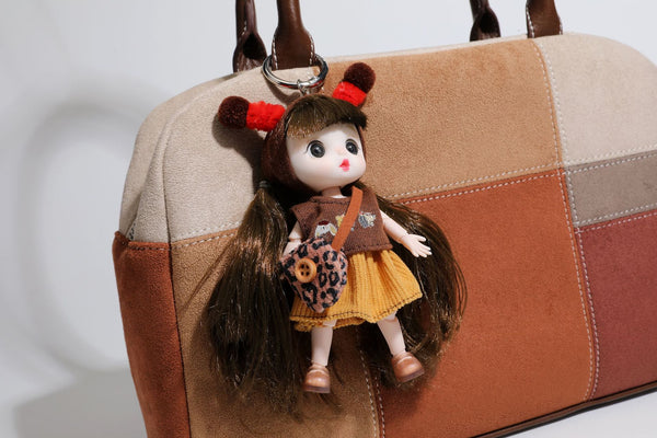 Boxy patchwork suede-look shoulder tote in tan, beige, rust, and brown panels with double brown straps and hanging doll
