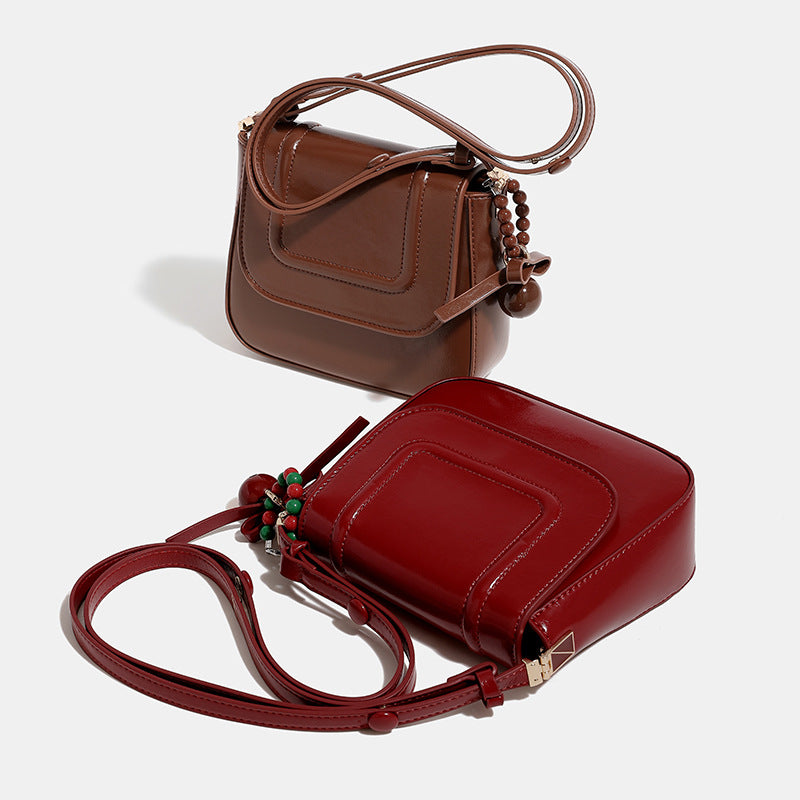 Mini glossy leather-look saddle crossbody bag with flap closure, gold-tone hardware, and beaded charm, detail view 2