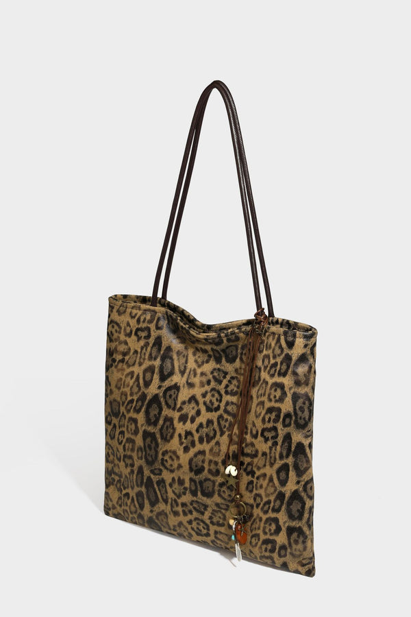 Large leopard print shoulder tote bag in tan and brown with slim dark straps and dangling beaded charm hardware, detail view