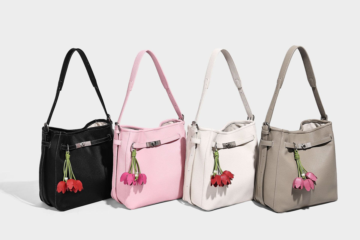 Soft-structured pebbled bucket shoulder bag with front turn-lock strap detail, adjustable strap, and hanging floral tassel