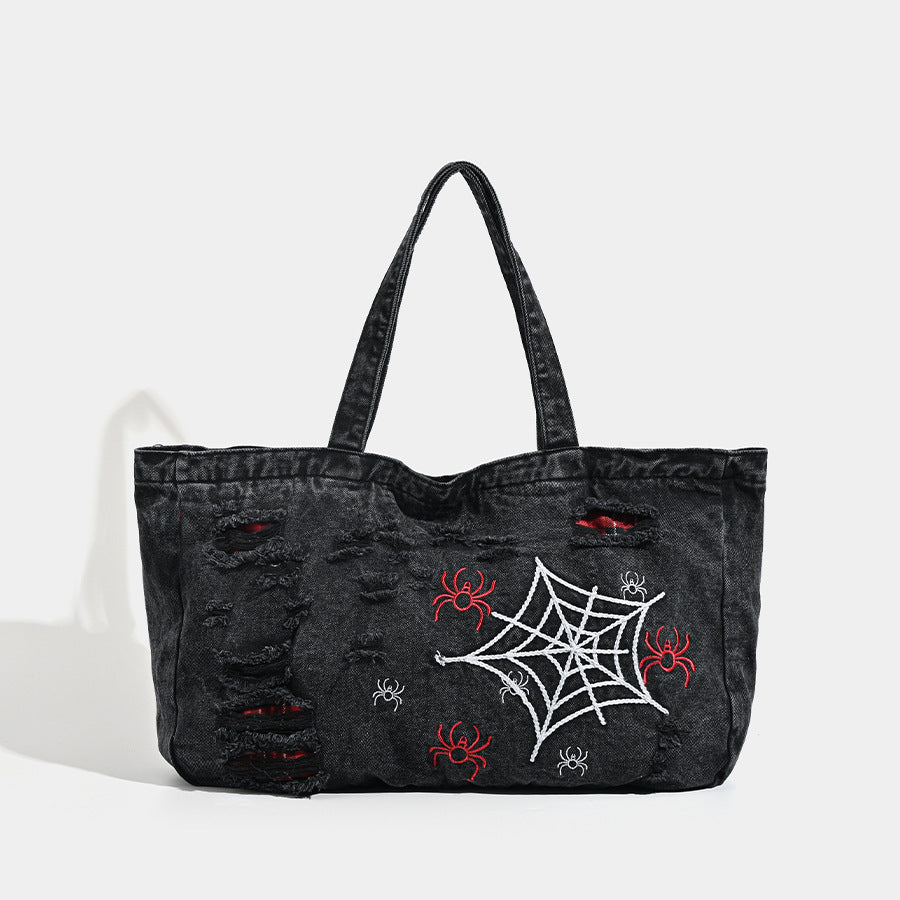 Large washed black distressed denim tote bag with white spider web embroidery and red spider motifs on the front panel
