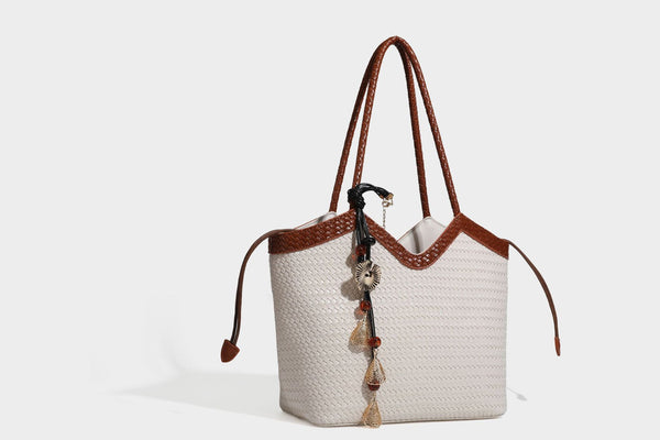 Olivgrüne Tote-Bag in Korbgeflecht-Optik mit dunkelbraunen geflochtenen Schulterriemen, seitlichen Kordelzügen und Perlenanhänger in Goldoptik