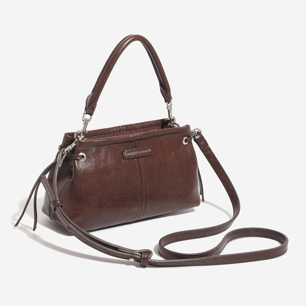 Small retro convertible shoulder bag with glossy leather-look finish, side drawstring ties, top zip closure, and silver-tone