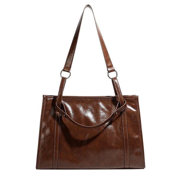 Large structured glossy leather-look tote bag with dual top handles and long shoulder strap in burnished brown, detail view 5