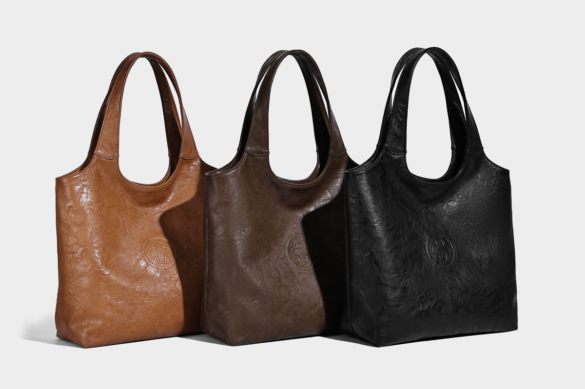 Large open-top tote bag with crinkled leather-look finish, long double shoulder straps, and embossed circular detail on