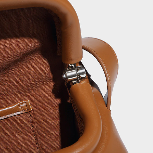 Compact structured baguette shoulder bag with smooth leather-look finish, zip top, and adjustable silver-buckle strap, detail