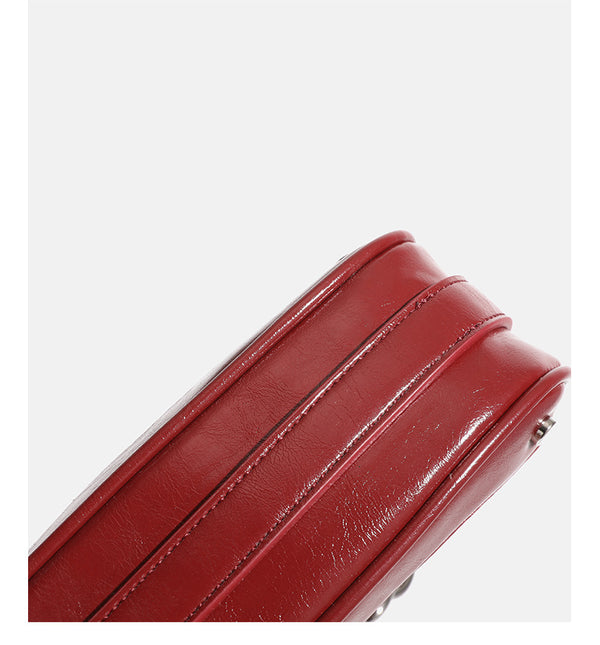 Small glossy cherry red crescent shoulder bag with silver chain strap, bead and tassel charm, and round pendant, detail view