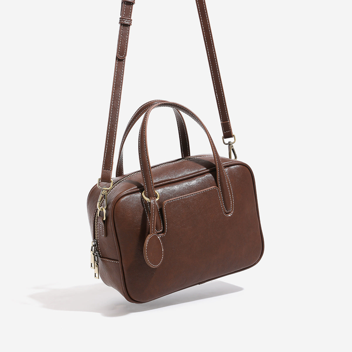 Structured boxy bowling-style tote bag in deep brown leather-look finish with dual top handles, front slip pocket, round