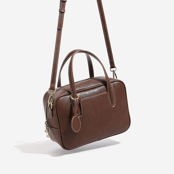 Structured boxy bowling-style tote bag in deep brown leather-look finish with dual top handles, front slip pocket, round