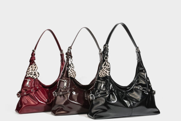 Glänzende dunkelbraune, lässig geschnittene Hobo-Schultertasche mit Riemendetail mit silberfarbenen Ösen, Reißverschlussfach auf der Vorderseite und Herz mit Leopardenmuster