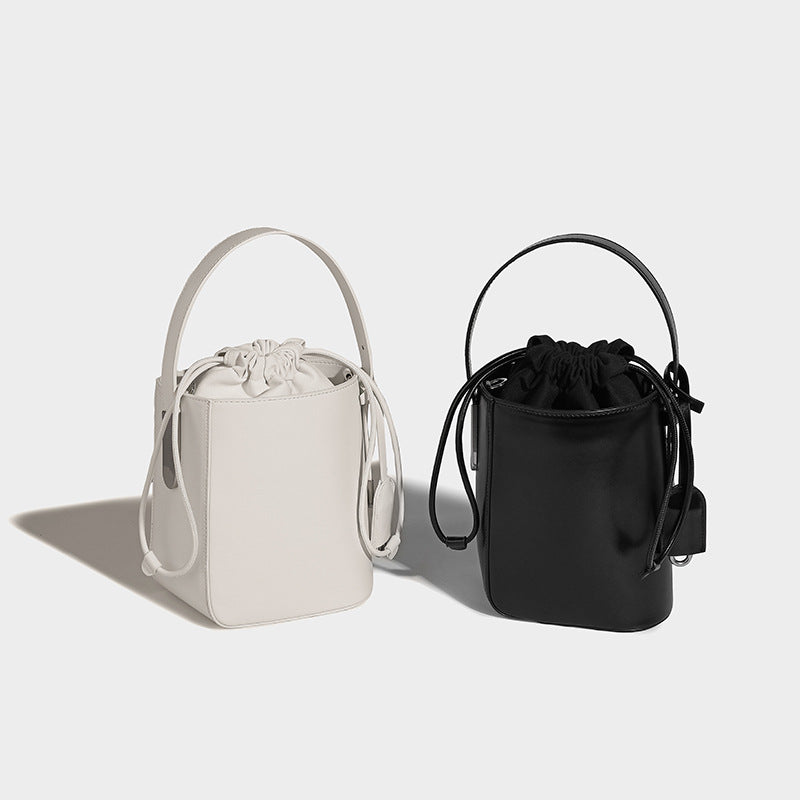 Small structured drawstring bucket bag in smooth matte leather-look finish with rigid top handle and detachable shoulder