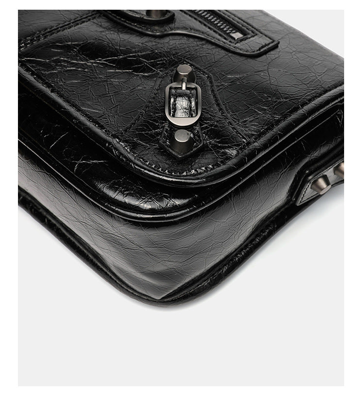 Small structured rectangular crossbody bag with crinkle leather-look finish, front zip pocket, gunmetal stud hardware, and