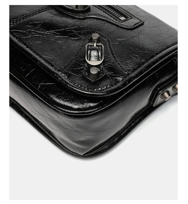 Small structured rectangular crossbody bag with crinkle leather-look finish, front zip pocket, gunmetal stud hardware, and