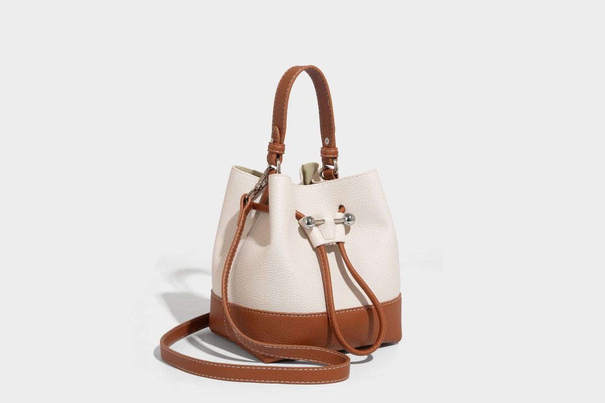Small two-tone pebbled drawstring bucket bag with tan contrast base, metal toggle hardware, short top handle, and detachable