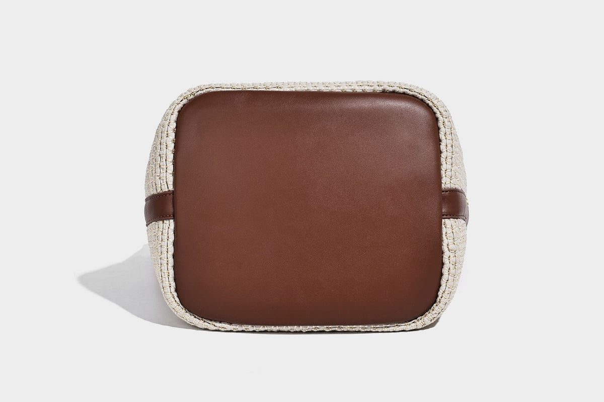 Woven straw-look tote bag in tan and cream with dark brown leather-look trim, long flat shoulder straps, and tassel bead