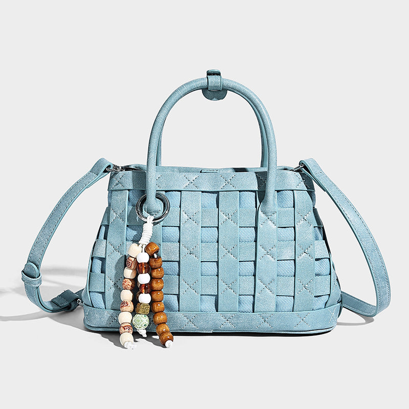 Small structured woven satchel tote with rounded top handles, silver-tone ring hardware, and bead tassel charm, detail view