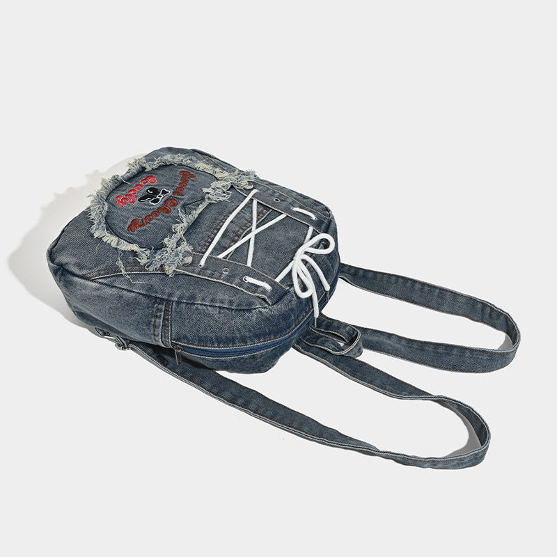 Rucksack aus gewaschenem blauem Denim mit weißer Schnürung auf der Vorderseite, ausgefranstem, herzförmigem besticktem Außenfach und Reißverschluss oben