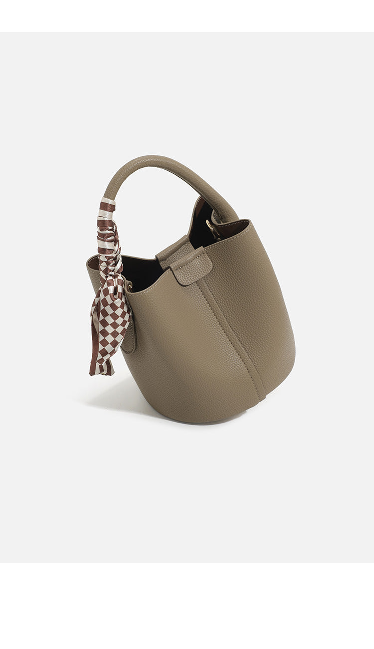 Pebbled leather-look bucket bag with checkered scarf-wrapped top handle, flap tab closure, gold-tone hardware, and matching