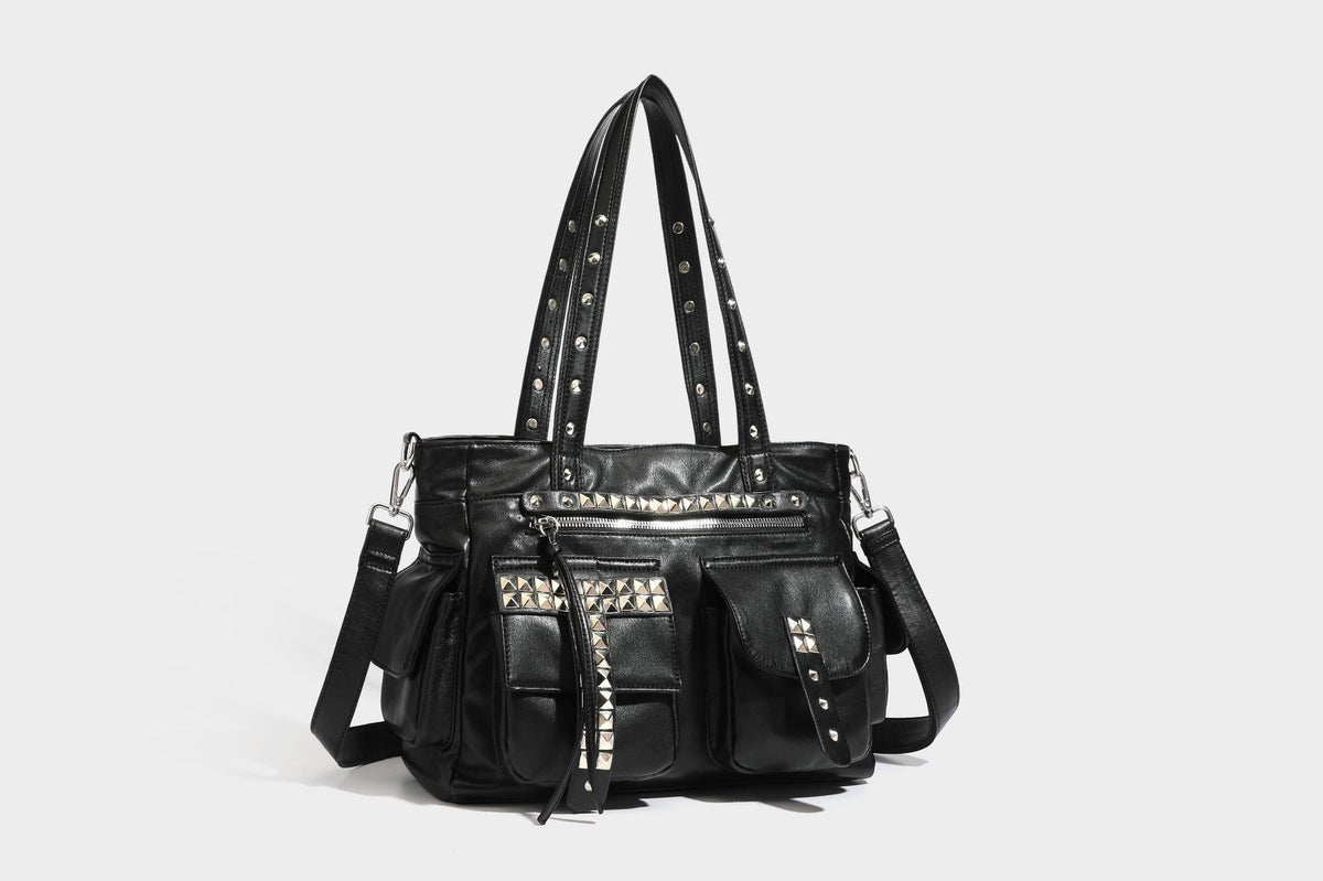 Black leather-look tote bag with silver pyramid studs on handles and front panel, multiple flap and zip exterior pockets