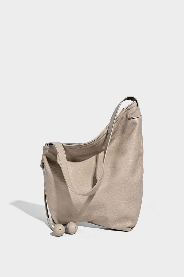 Slouchy hobo shoulder bag in pale yellow with slim strap, drawstring bead closure, and pink tulip floral charm, detail view