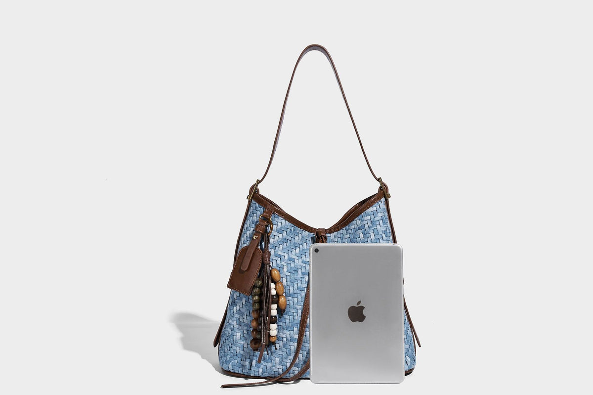 Light blue woven bucket bag with brown leather-look trim, gold-tone hardware, adjustable shoulder strap, and decorative bead