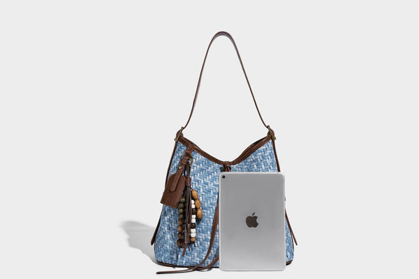 Light blue woven bucket bag with brown leather-look trim, gold-tone hardware, adjustable shoulder strap, and decorative bead