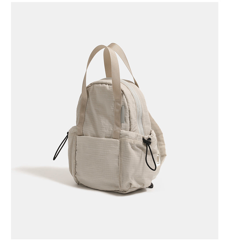 Small rounded mini backpack handbag in matte ripstop-texture fabric with top webbing handle, front pocket, side drawstring