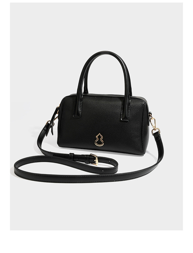 Small structured pillow satchel bag with pebbled leather-look finish, dual rolled top handles, gold-tone gourd emblem, and