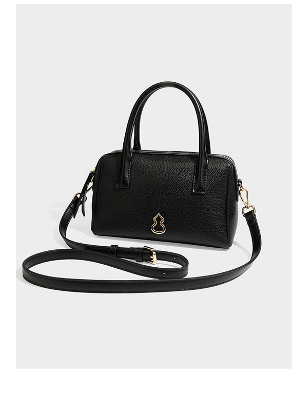 Small structured pillow satchel bag with pebbled leather-look finish, dual rolled top handles, gold-tone gourd emblem, and