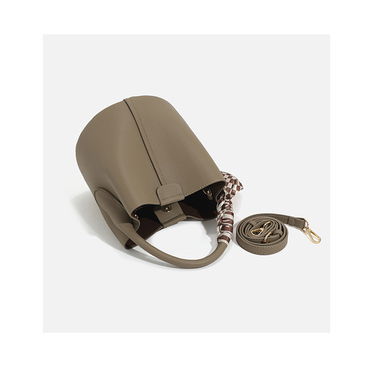 Pebbled leather-look bucket bag with checkered scarf-wrapped top handle, flap tab closure, gold-tone hardware, and matching