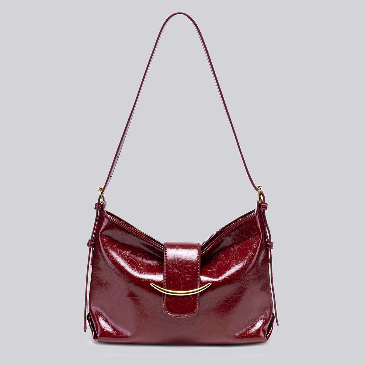 Glossy burgundy leather-look shoulder bag with curved gold-tone bar front closure, crinkled oil-wax texture, and adjustable