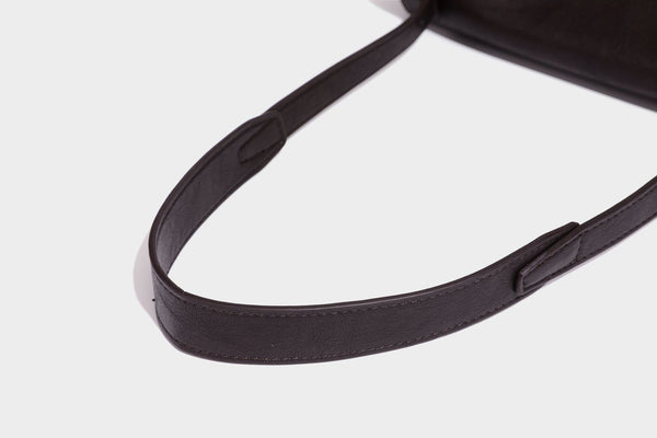 Strukturierte rechteckige dunkelbraune Schultertasche in Lederoptik mit Klappe, mehrlagigem Detail auf der Vorderseite und langem verstellbarem Riemen, Detailansicht