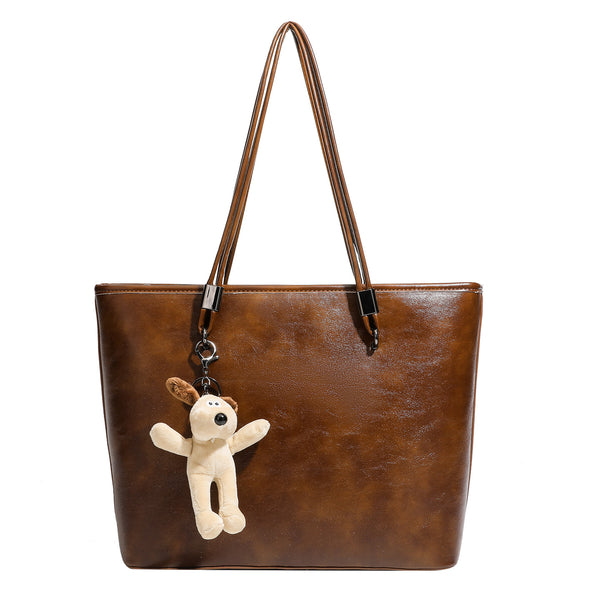 Large structured brown vintage-finish tote bag with double shoulder handles, gunmetal hardware, and plush bear charm, detail