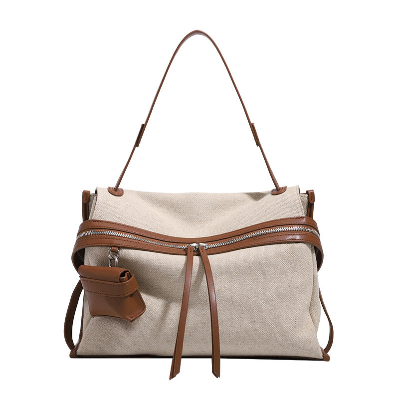 Cream canvas zip-top shoulder bag with cognac leather-look trim, dual zipper, attached mini pouch, and tassel strap ties